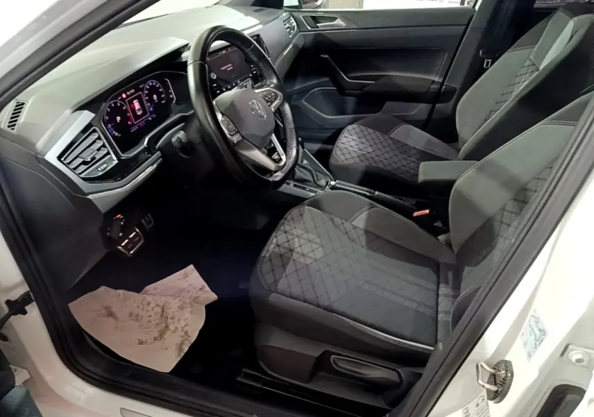 Vue intérieure côté conducteur d'un Volkswagen Taigo blanc 2022, volant cuir alu multifonctions et sièges tissu gris à motifs.