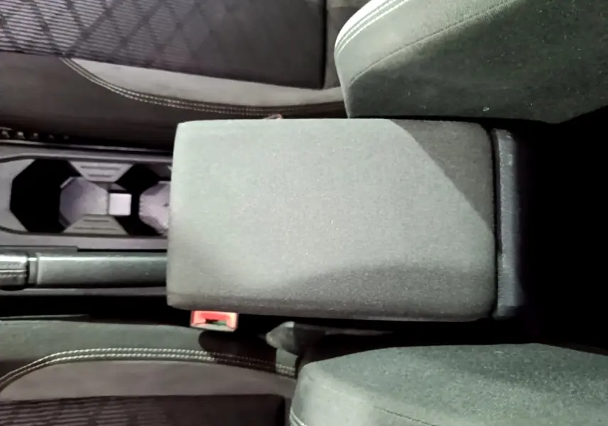 Vue plongeante sur l'accoudoir central noir et les sièges avant en tissu du Volkswagen Taigo blanc 2022.