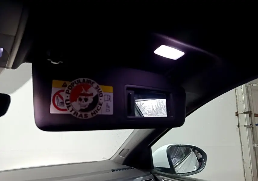 Vue intérieure côté conducteur du pare-soleil avec miroir éclairé et rétroviseur extérieur blanc d’un Volkswagen Taigo blanc.