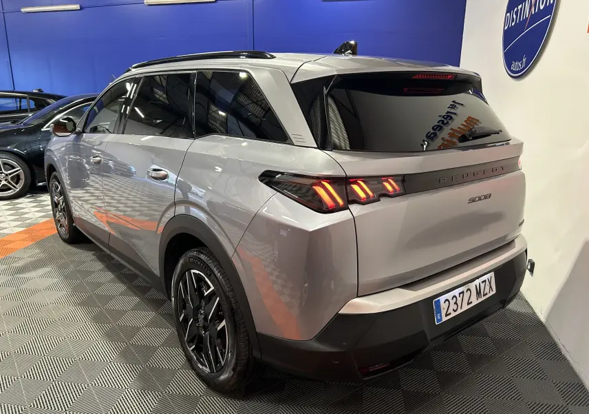 Vue 3/4 arrière droite du Peugeot 5008 gris Artense avec feux arrière allumés dans un showroom.