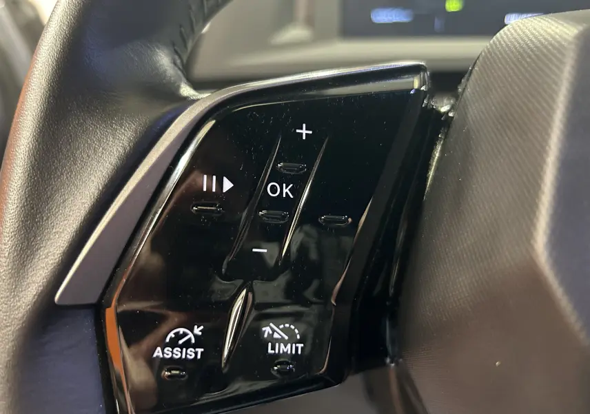 Gros plan sur les commandes noires du volant côté gauche du Peugeot 5008 hybride gris Artense, avec boutons de réglage et assistance.