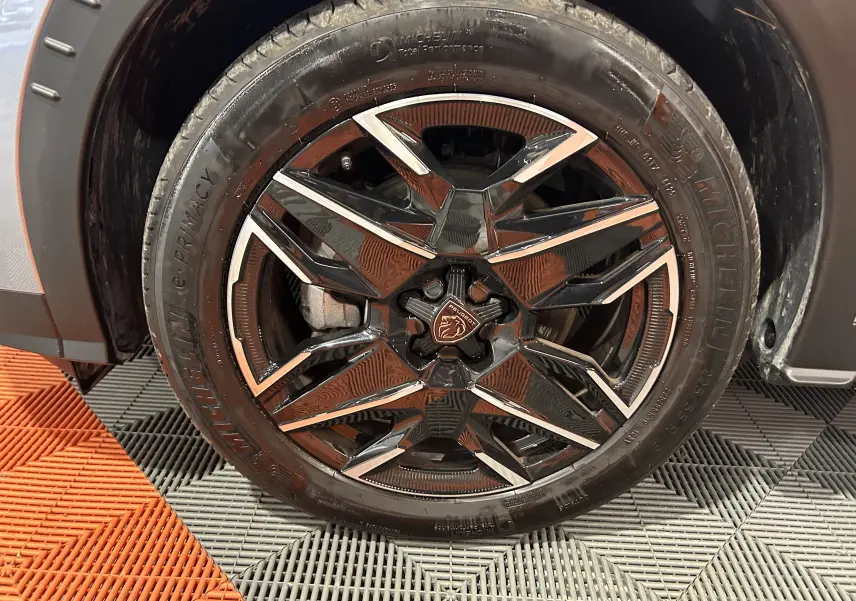 Gros plan sur la roue avant gauche du Peugeot 5008 gris Artense, mettant en valeur la jante noire et argentée au design moderne.