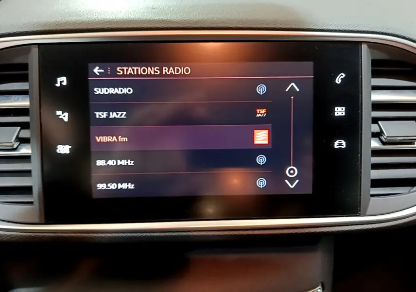Écran tactile central affichant les stations radio dans l'habitacle d'une Peugeot 308 gris clair, vue de face.