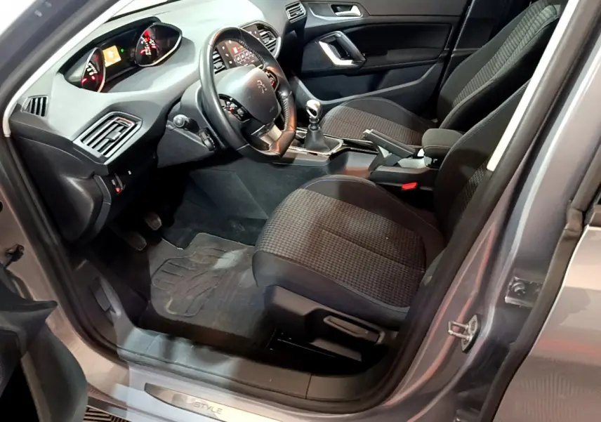 Intérieur côté conducteur d'une Peugeot 308 gris clair 2020, volant cuir, boîte manuelle et tableau de bord digital.