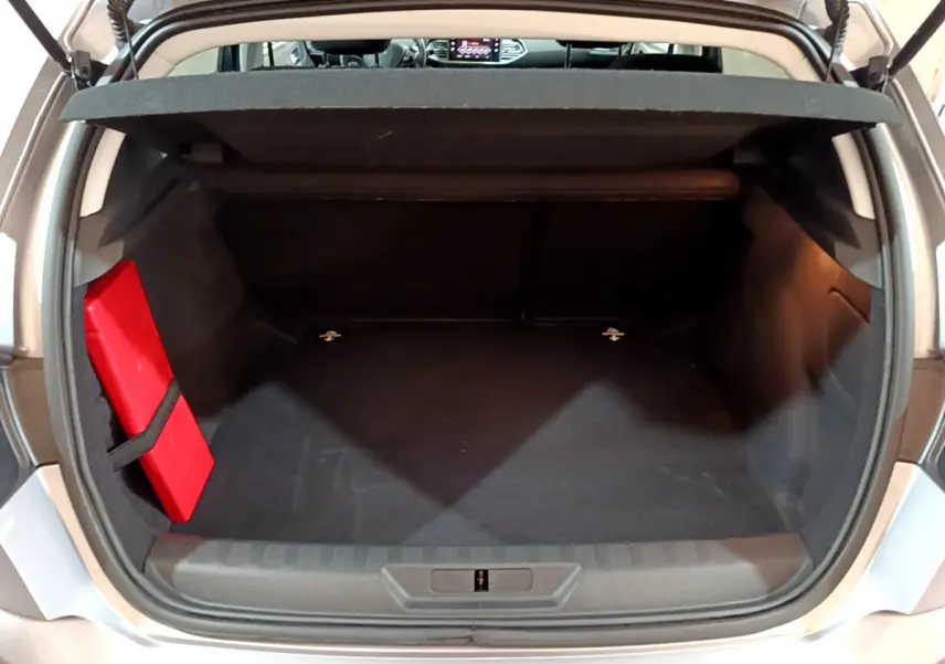 Coffre ouvert d'une Peugeot 308 gris clair, montrant un espace de rangement avec un triangle de signalisation rouge fixé à gauche.