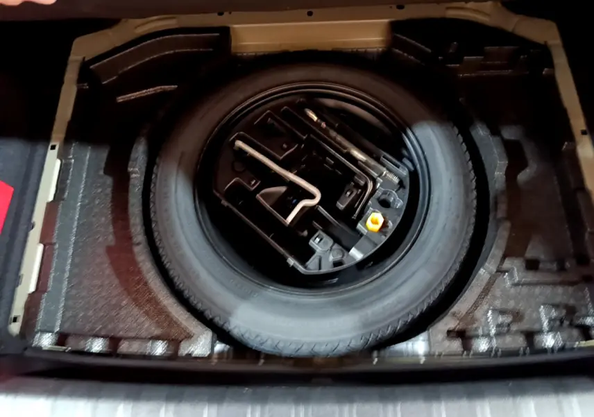 Vue plongeante sur la roue de secours et les outils de bord dans le coffre d'une Peugeot 308 gris clair 2020.