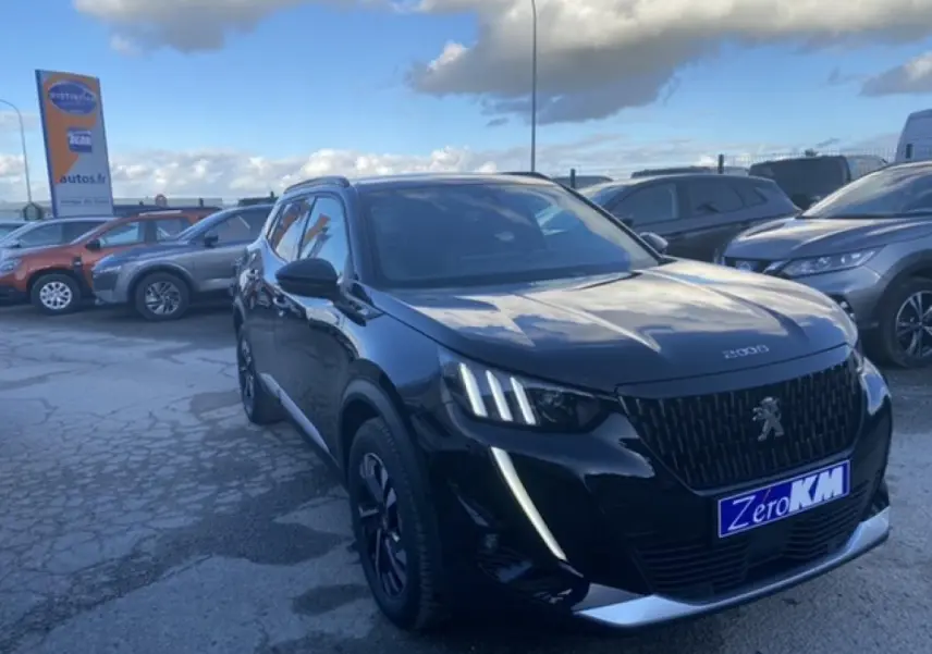 Peugeot 2008 noir vue 3/4 avant droit, avec calandre distinctive et feux LED verticaux allumés sur parking extérieur.