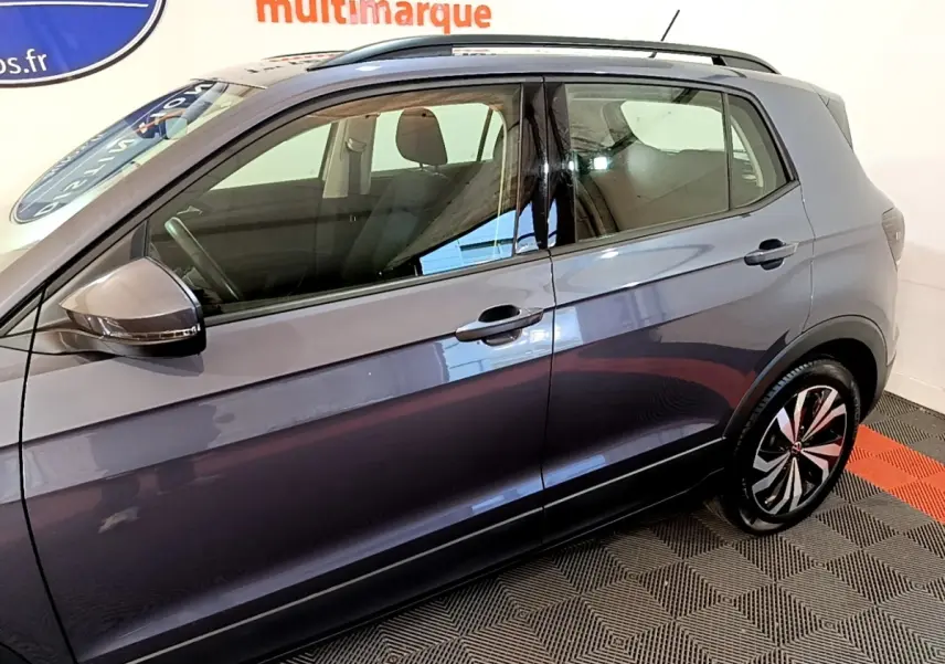 Vue de profil côté gauche du Volkswagen T-Cross gris foncé 2023 avec jantes alliage et barres de toit noires.