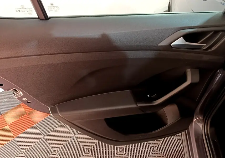 Vue intérieure de la porte avant gauche du Volkswagen T-Cross gris foncé, avec poignée et commande de vitre visible.