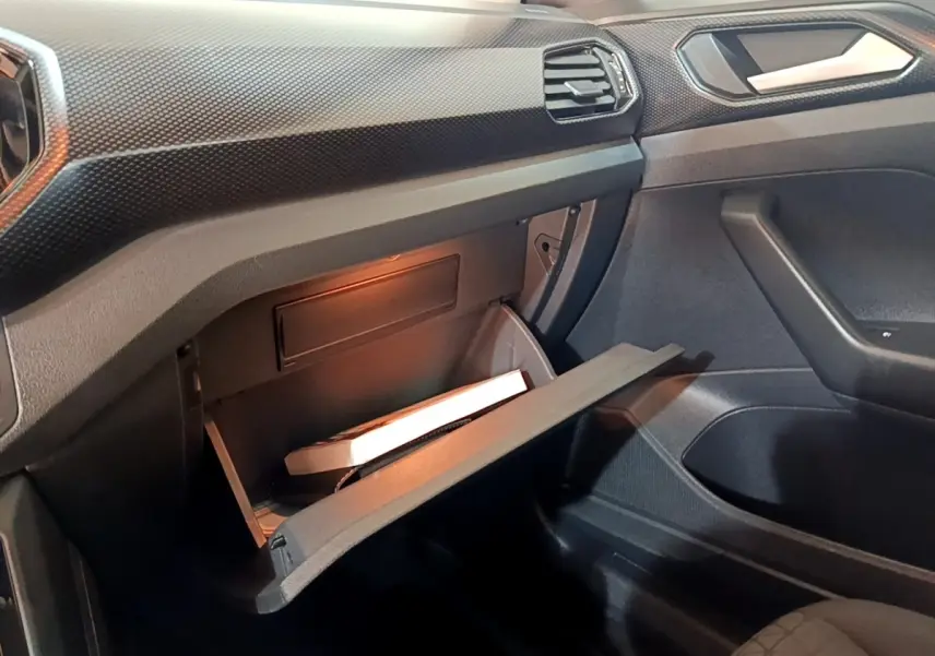 Vue intérieure côté passager du Volkswagen T-Cross 2023 gris foncé, boîte à gants ouverte avec éclairage intérieur.