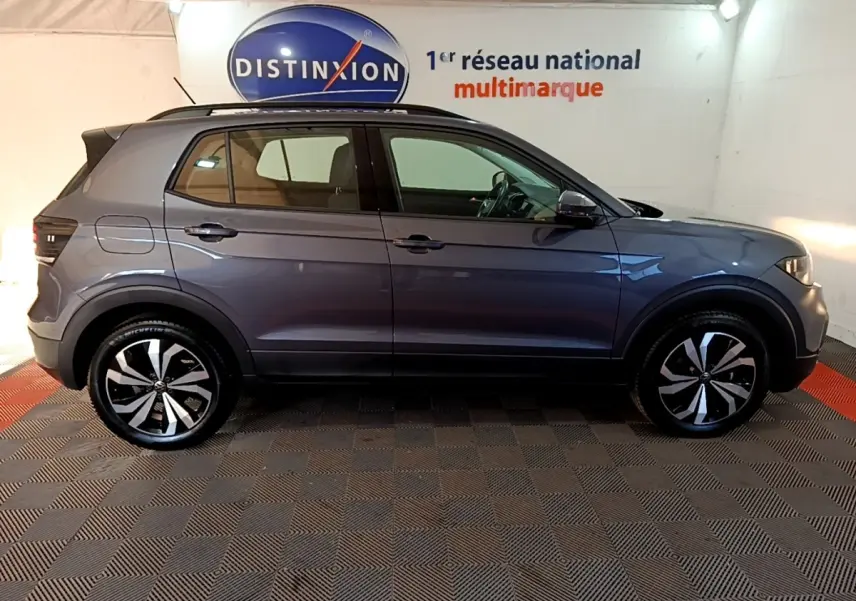 Profil côté gauche d'un Volkswagen T-Cross gris foncé 2023 avec jantes alliage distinctives dans un showroom.