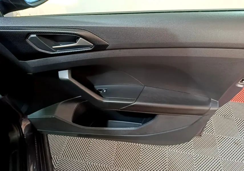 Vue intérieure côté gauche de la porte d’un Volkswagen T-Cross 2023 gris foncé avec poignée et rangement intégré.