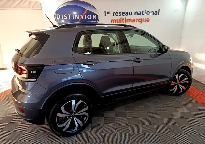 Vue 3/4 arrière droite d'un Volkswagen T-Cross gris foncé avec jantes alliage et feux LED, en intérieur showroom.
