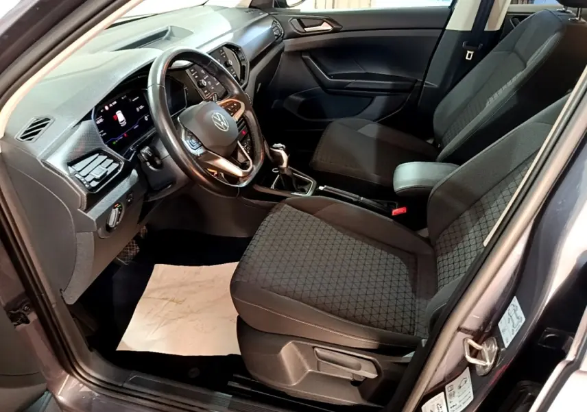 Vue intérieure côté conducteur du Volkswagen T-Cross gris foncé 2023, volant cuir multifonctions et sièges tissu noirs.