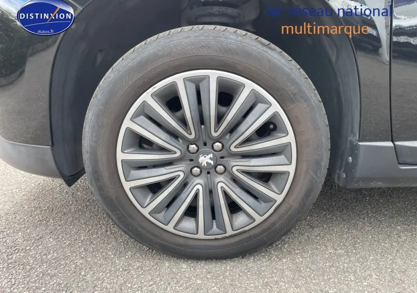 Gros plan sur la roue avant gauche d'un Peugeot 2008 noir métal, mettant en valeur la jante au design moderne.