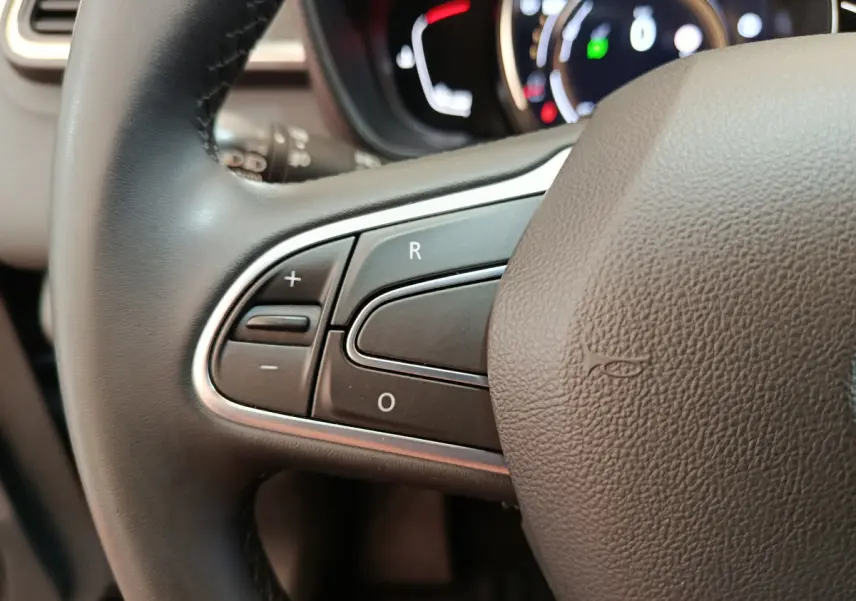 Gros plan sur les commandes au volant côté gauche du Renault Kadjar Business gris foncé, tableau de bord en arrière-plan flou.