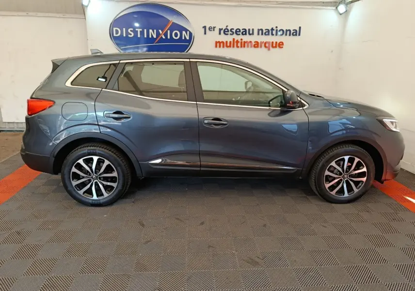Profil côté gauche d'un Renault Kadjar Business gris foncé, stationné en intérieur avec jantes alliage et logo Distinxion en arrière-plan.