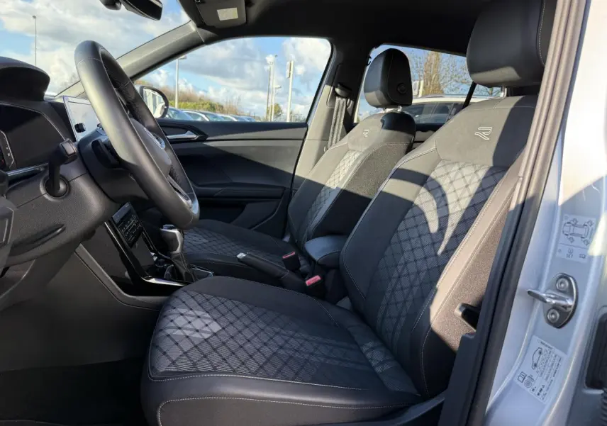 Intérieur avant droit du Volkswagen T-Cross 2025 argent, sièges R-Line en tissu noir à motifs losanges.