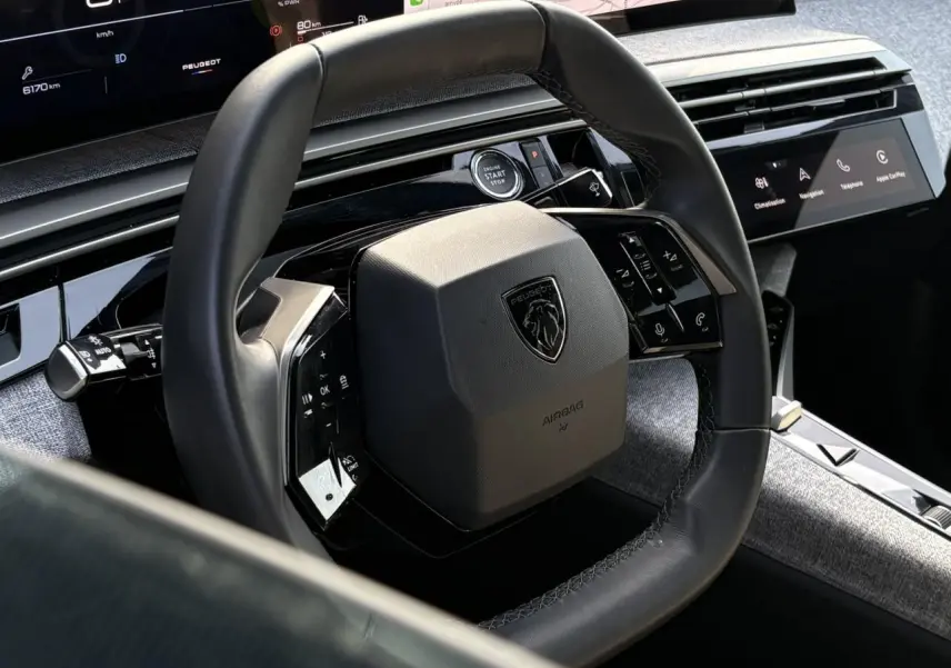 Vue rapprochée du volant cuir noir et du tableau de bord numérique du Peugeot 3008 Hybrid blanc Okenite 2025.