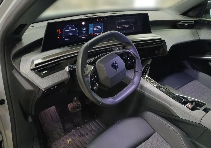 Vue intérieure côté conducteur du Peugeot 3008 Hybrid 2025, volant compact cuir noir et tableau de bord numérique panoramique.