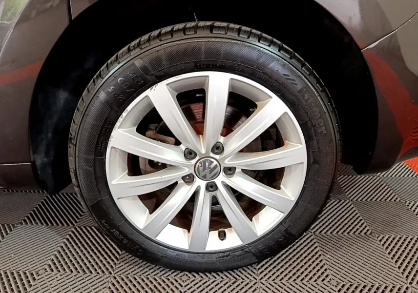 Gros plan sur la roue avant droite d’un Volkswagen Sharan marron, avec jante alliage argentée et logo VW central.