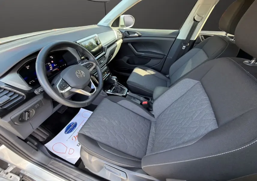 Vue intérieure côté conducteur du Volkswagen T-Cross 2025, sellerie tissu noir avec tableau de bord moderne.
