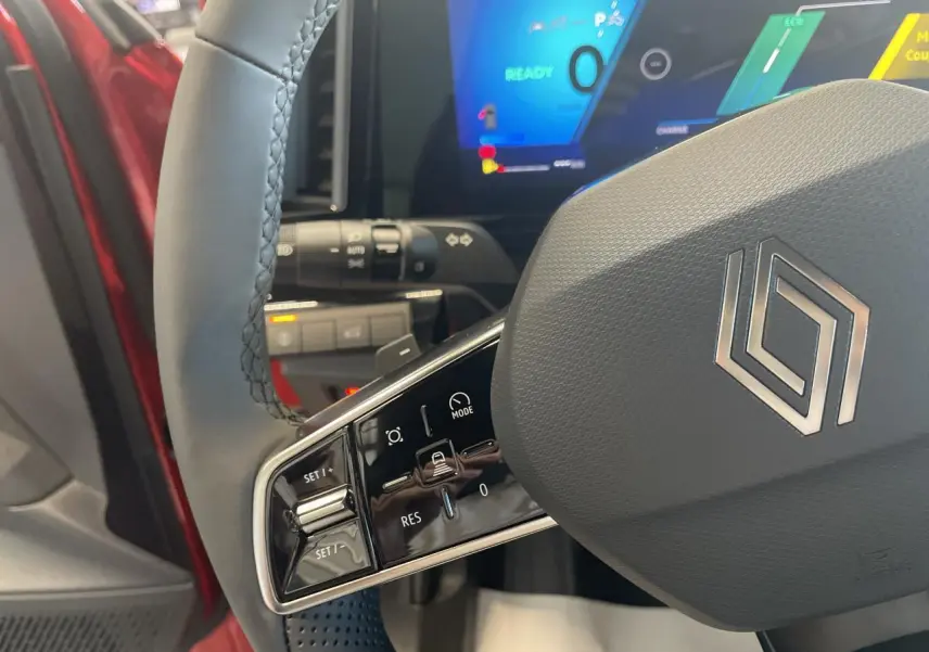 Gros plan sur le volant textile refined gris du Renault Rafale 2025 rouge, avec commandes intégrées et tableau de bord numérique.