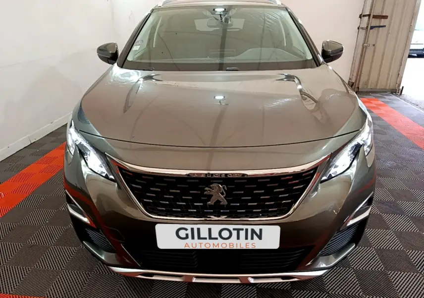 Vue frontale d'un Peugeot 3008 gris clair avec calandre chromée et phares LED allumés dans un garage.