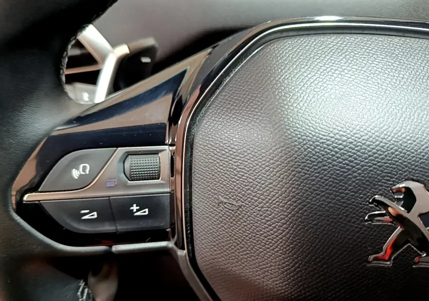 Gros plan sur le volant cuir noir du Peugeot 3008 2020 avec commandes vocales et logo lion chromé visible.