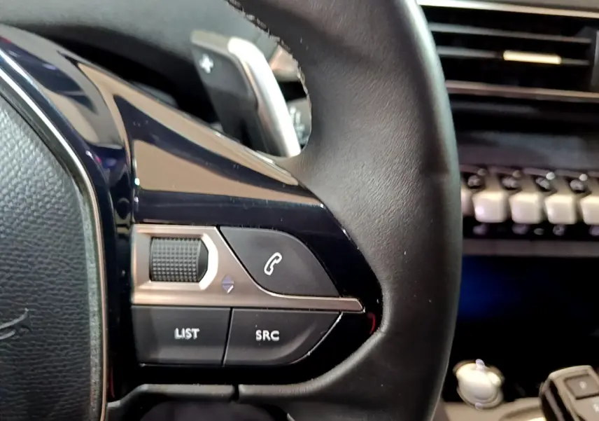 Gros plan sur les commandes gauche du volant cuir noir du Peugeot 3008 gris clair, avec tableau de bord en arrière-plan.