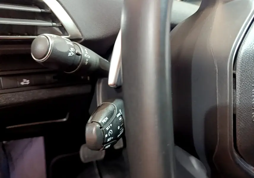 Gros plan sur les commandes au volant noir du Peugeot 3008 gris clair, côté gauche du tableau de bord.