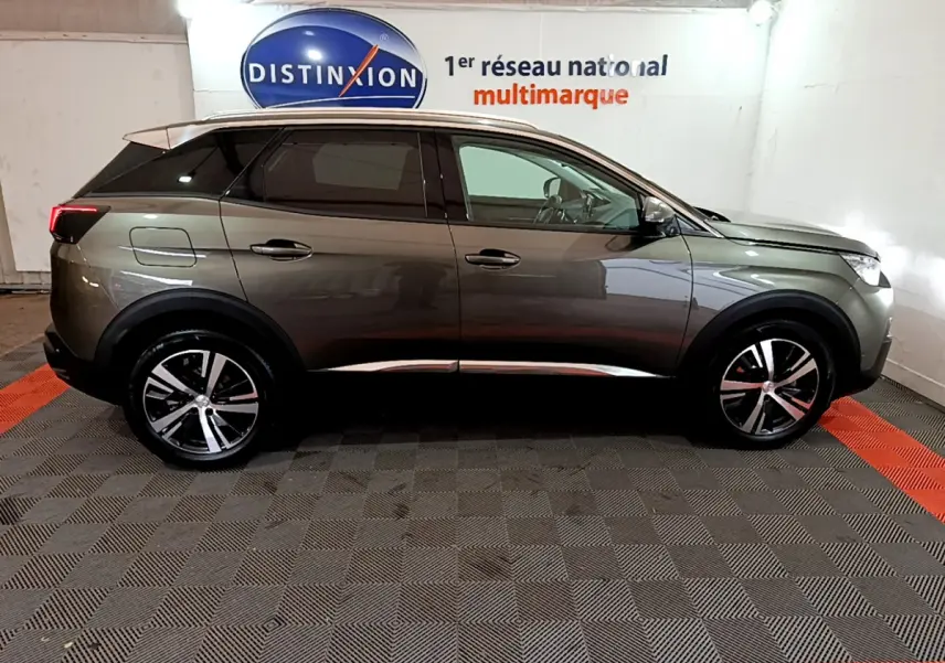 Profil côté gauche du Peugeot 3008 gris clair 2020, avec jantes alliage et vitres teintées en arrière-plan showroom.