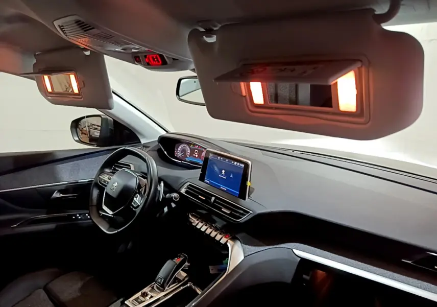 Intérieur du Peugeot 3008 gris clair vu côté conducteur, tableau de bord moderne avec écran tactile allumé et miroirs de courtoisie éclairés.