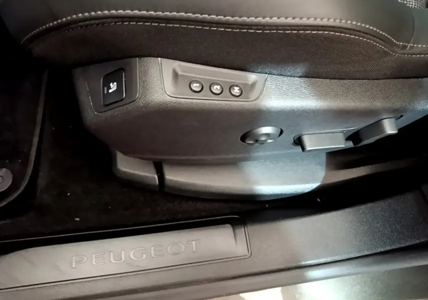 Gros plan sur les commandes de réglage du siège côté conducteur et seuil de porte Peugeot noir dans un intérieur sombre.
