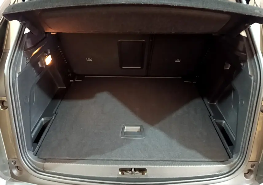 Coffre ouvert vu de l'arrière d'un Peugeot 3008 gris clair, avec espace de chargement propre et éclairage latéral allumé.