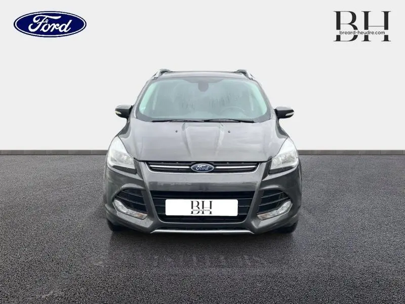 Vue de face d'un Ford Kuga gris Magnetic 2015 avec calandre chromée et phares halogènes allumés.