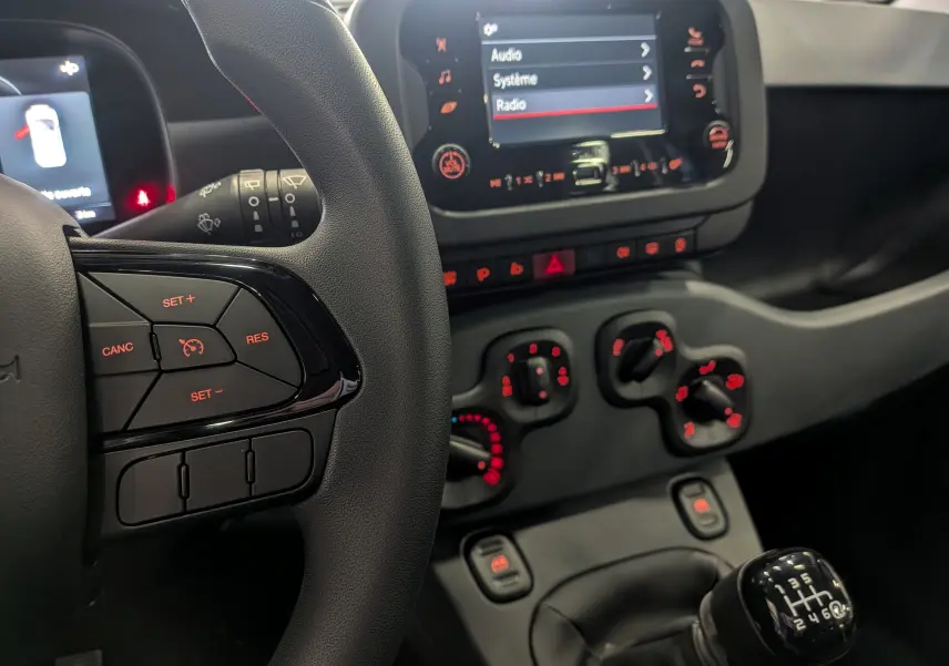 Vue rapprochée de l'intérieur de la Fiat Panda 2025 Bleu Italia, montrant le volant, la console centrale et le levier de vitesses manuel.