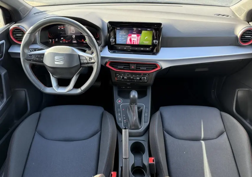 Vue intérieure frontale du tableau de bord et des sièges noirs de la SEAT IBIZA 2024 avec volant sport et écran tactile central.