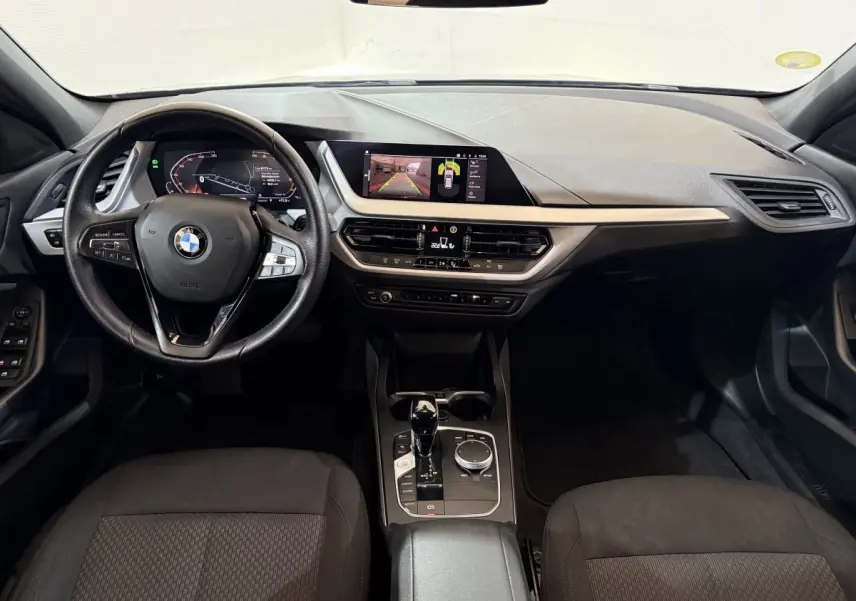 Vue intérieure avant de la BMW Série 1 116d Business Design 2022, tableau de bord noir avec écran tactile et volant cuir multifonctions.