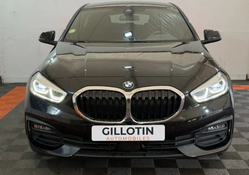 Vue avant d'une BMW Série 1 116d noire avec phares LED allumés et calandre double haricot chromée.