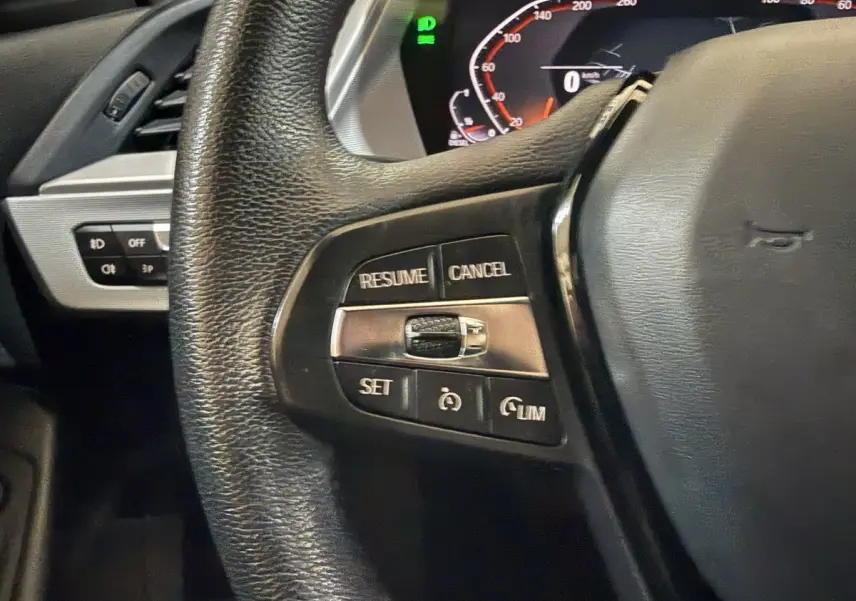 Gros plan sur le côté gauche du volant cuir noir d'une BMW Série 1 116d 2022 avec commandes du régulateur de vitesse.