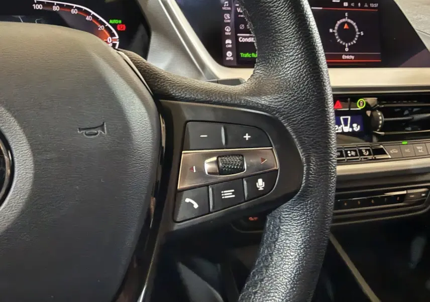 Gros plan sur le volant cuir noir de la BMW Série 1 116d avec commandes multifonctions et tableau de bord digital.