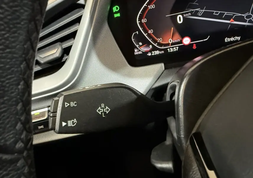 Gros plan sur le commodo gauche du tableau de bord d’une BMW Série 1 116d noir, avec affichage digital et témoin vert allumé.