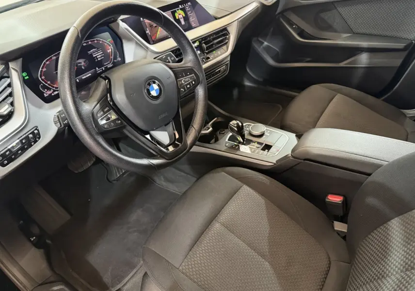 Vue intérieure côté conducteur de la BMW Série 1 116d Business Design 2022 avec tableau de bord digital et volant cuir noir.