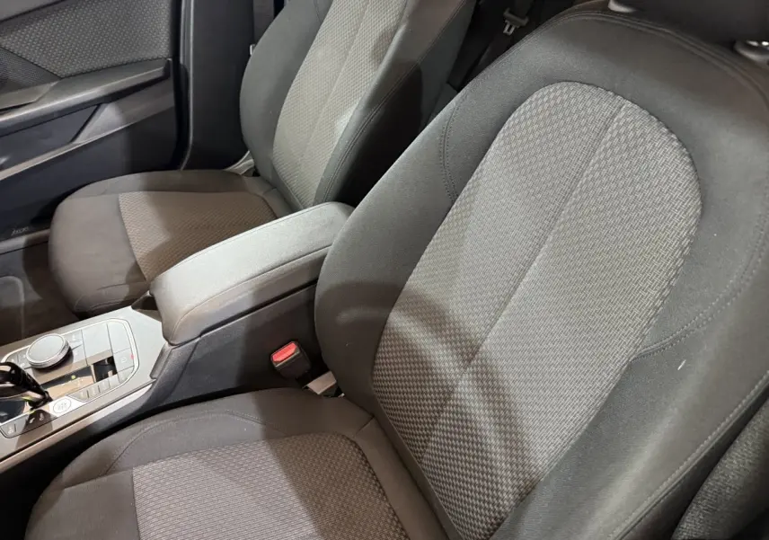 Vue rapprochée des sièges avant tissu gris et console centrale de la BMW Série 1 116d Business Design noire 2022.