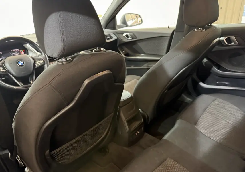 Vue intérieure arrière de la BMW Série 1 116d Business Design noire, montrant les sièges et le tableau de bord avant.