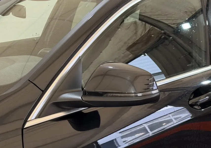 Gros plan sur le rétroviseur côté gauche d’une BMW Série 1 noire, avec poignée de porte et contours chromés visibles.