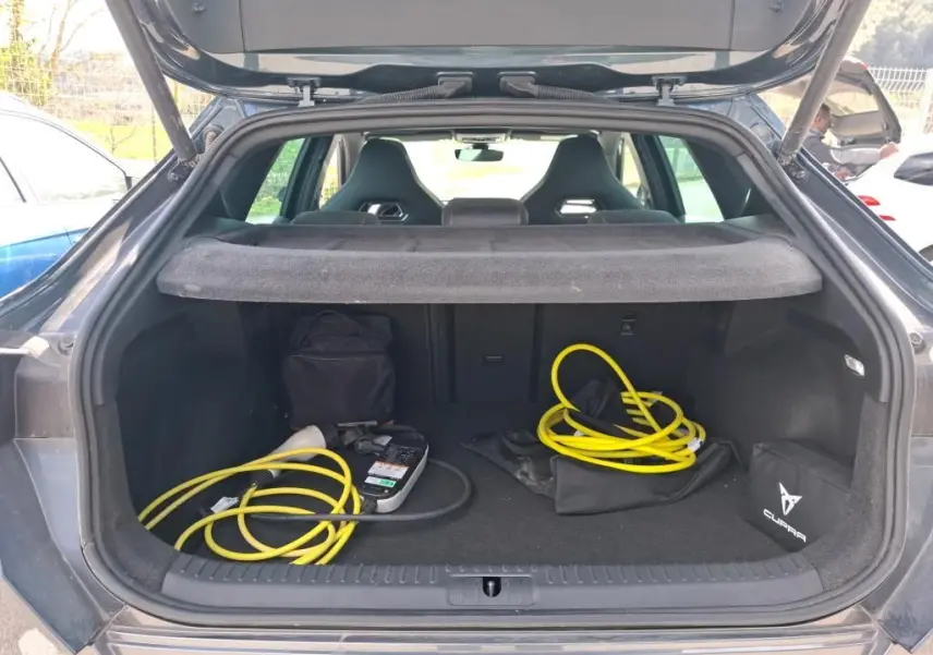 Coffre ouvert d'une CUPRA Formentor gris clair 2024, vue arrière, avec câbles de recharge jaune et sac de marque visible.