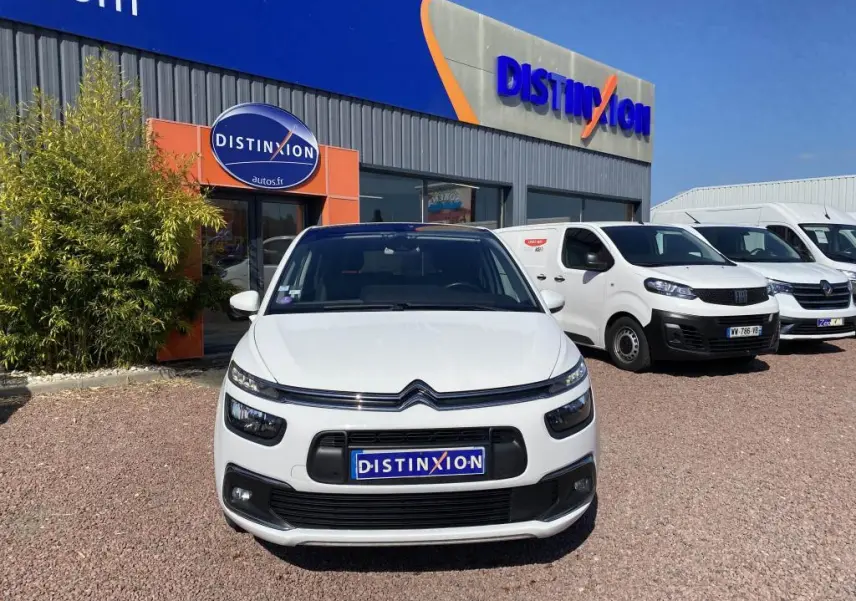 Vue de face d'une Citroën C4 Spacetourer blanche garée devant un concessionnaire Distinxion par temps ensoleillé.