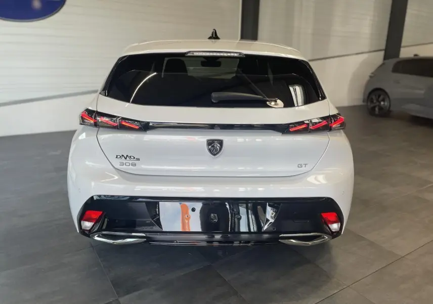 Vue arrière d'une Peugeot 308 GT blanche avec feux arrière à signature lumineuse griffe à griffe et diffuseur noir brillant.